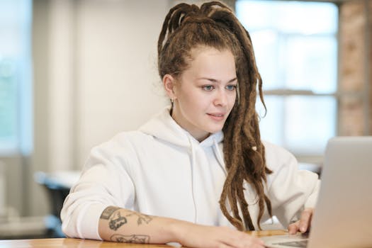 一位留着辫子、纹身的女性在休闲环境中专注于使用笔记本电脑工作