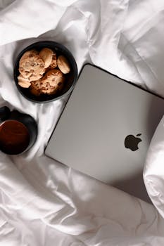 A cozy setup on a bed with a tablet, coffee cup, and bowl of cookies, ideal for relaxation.