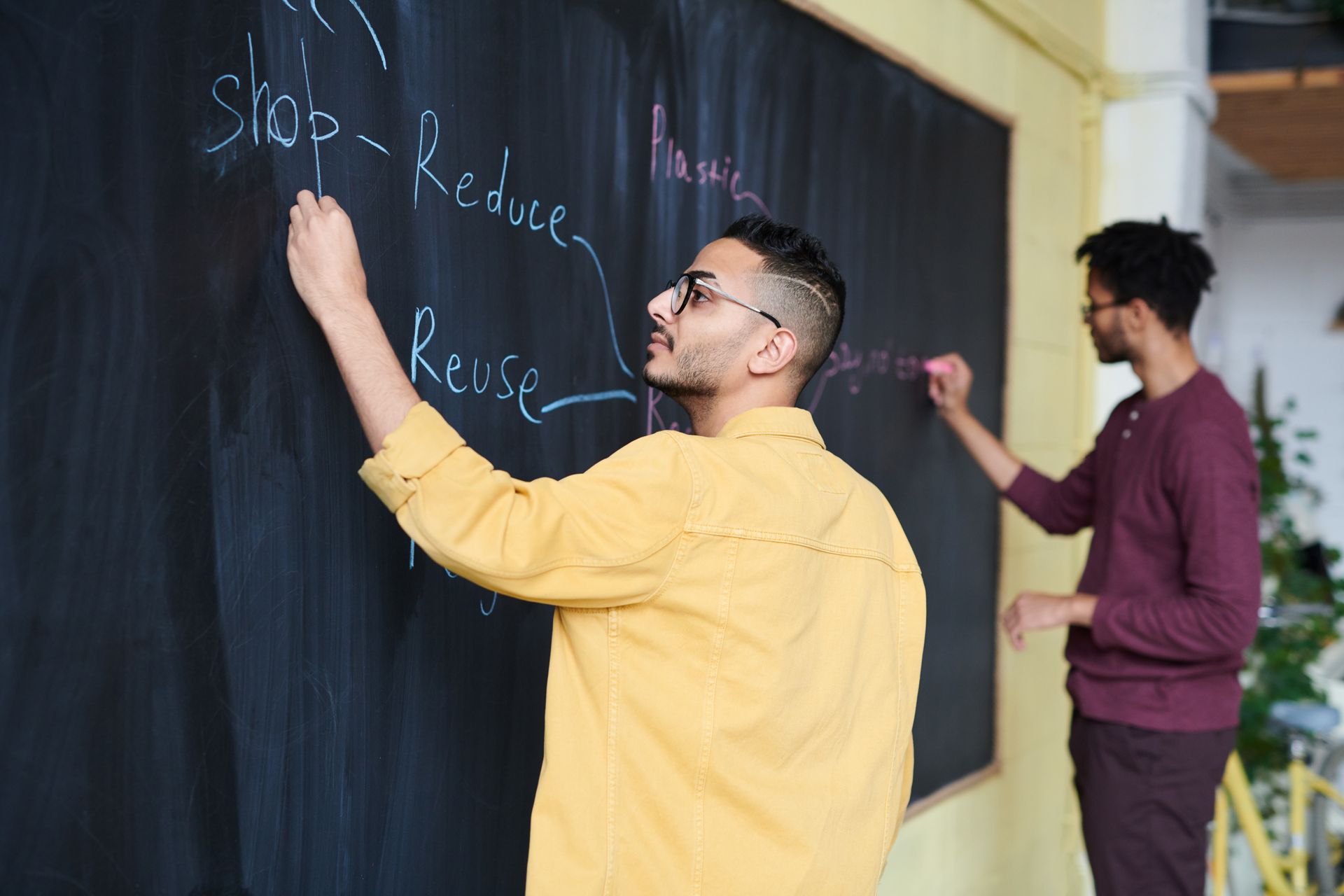 Two young men writing on a chalkboard, illustrating a mind map indoors.