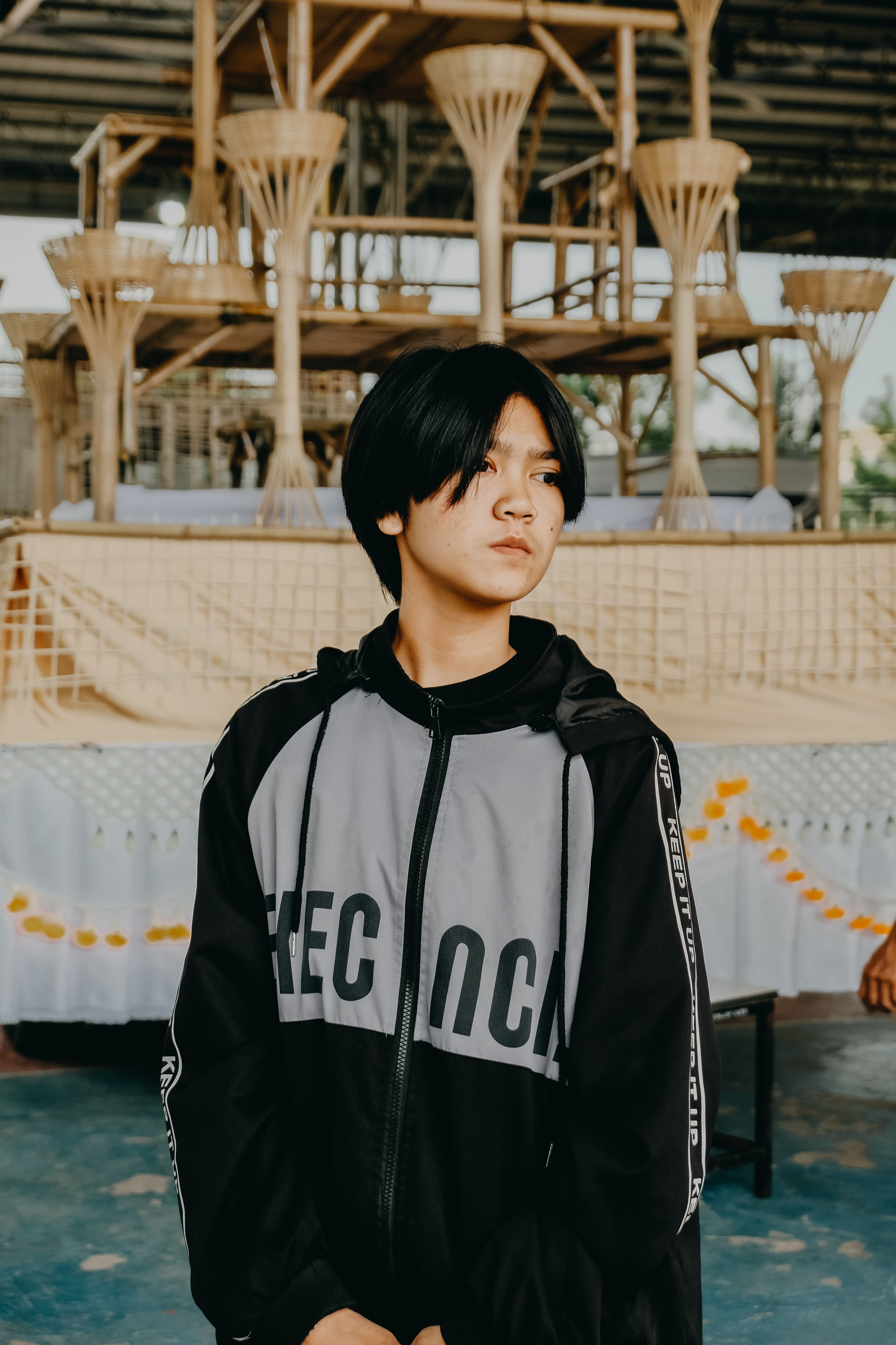 Young individual in a casual hoodie standing indoors with unique wood structures in the background.