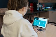 一名身穿白色连帽衫的女子在舒适的咖啡馆里，正专注地在笔记本电脑上工作