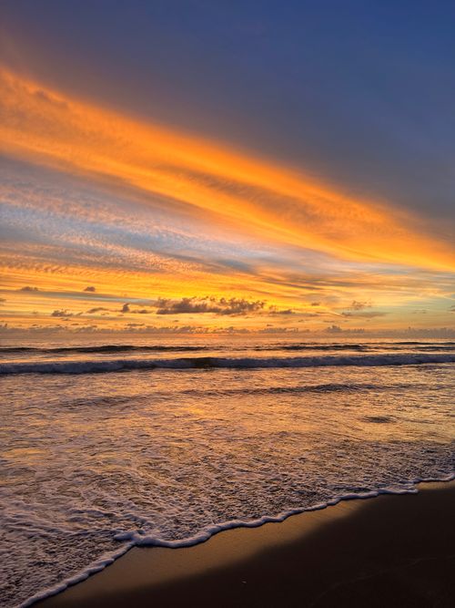 Free Dramatic sunset over the ocean with vibrant orange and blue sky. Perfect for travel and nature themes. Stock Photo