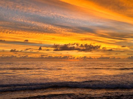 Experience a vibrant sunset painting the ocean waves in warm hues of orange and yellow.