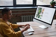 一名穿着休闲装的年轻人，正在一间现代时尚的办公室里，坐在木桌前用电脑工作