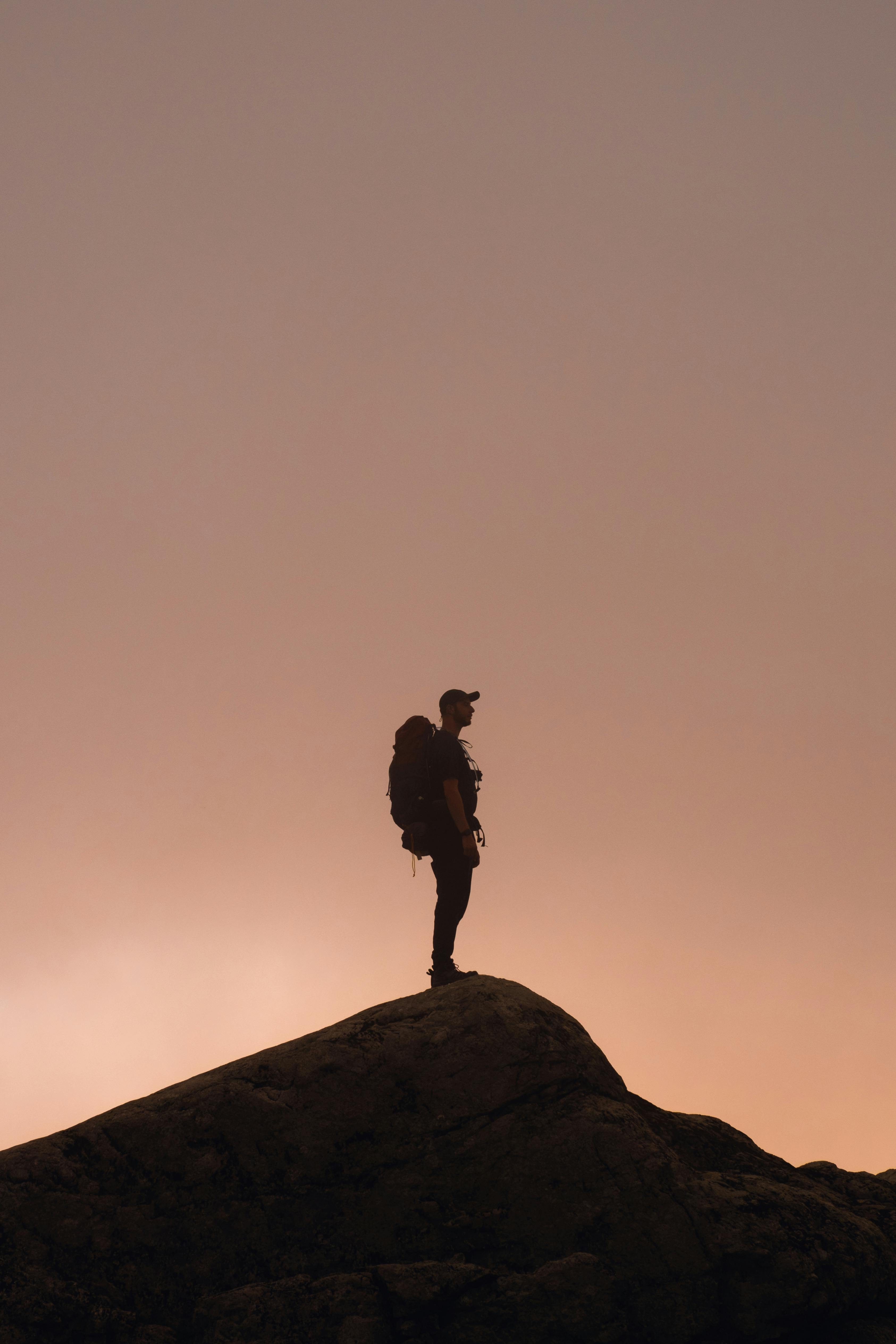 在山峰之上，一个孤独的徒步旅行者的身影映衬着戏剧性的日落天空，象征着冒险