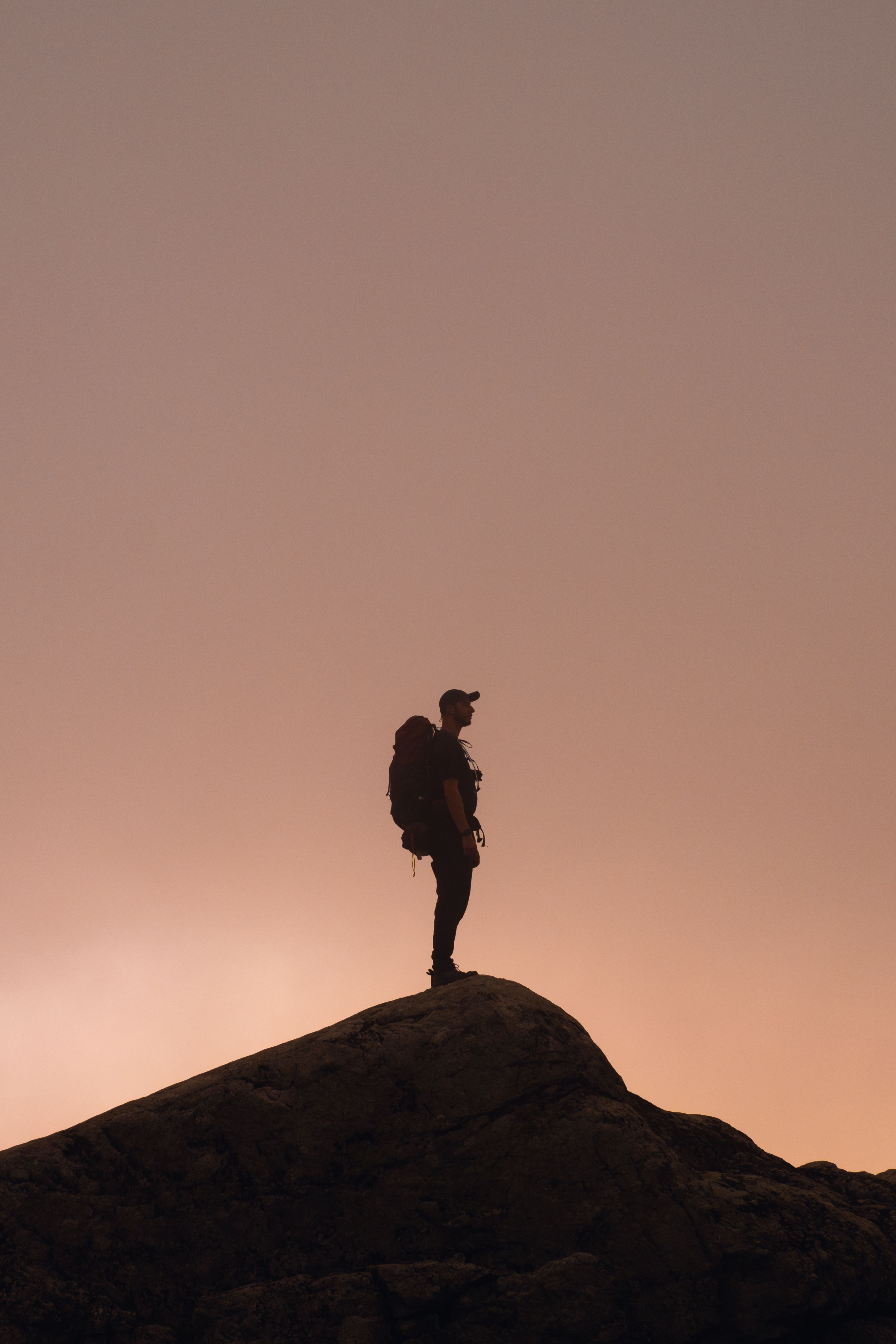 Kostenlos Die Silhouette eines einsamen Wanderers vor einem dramatischen Sonnenuntergangshimmel auf einem Berggipfel symbolisiert Abenteuer. Stock-Foto