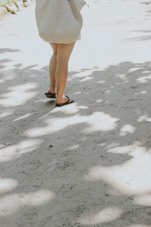 Free Person strolling on sandy beach path with light and shadow play. Stock Photo