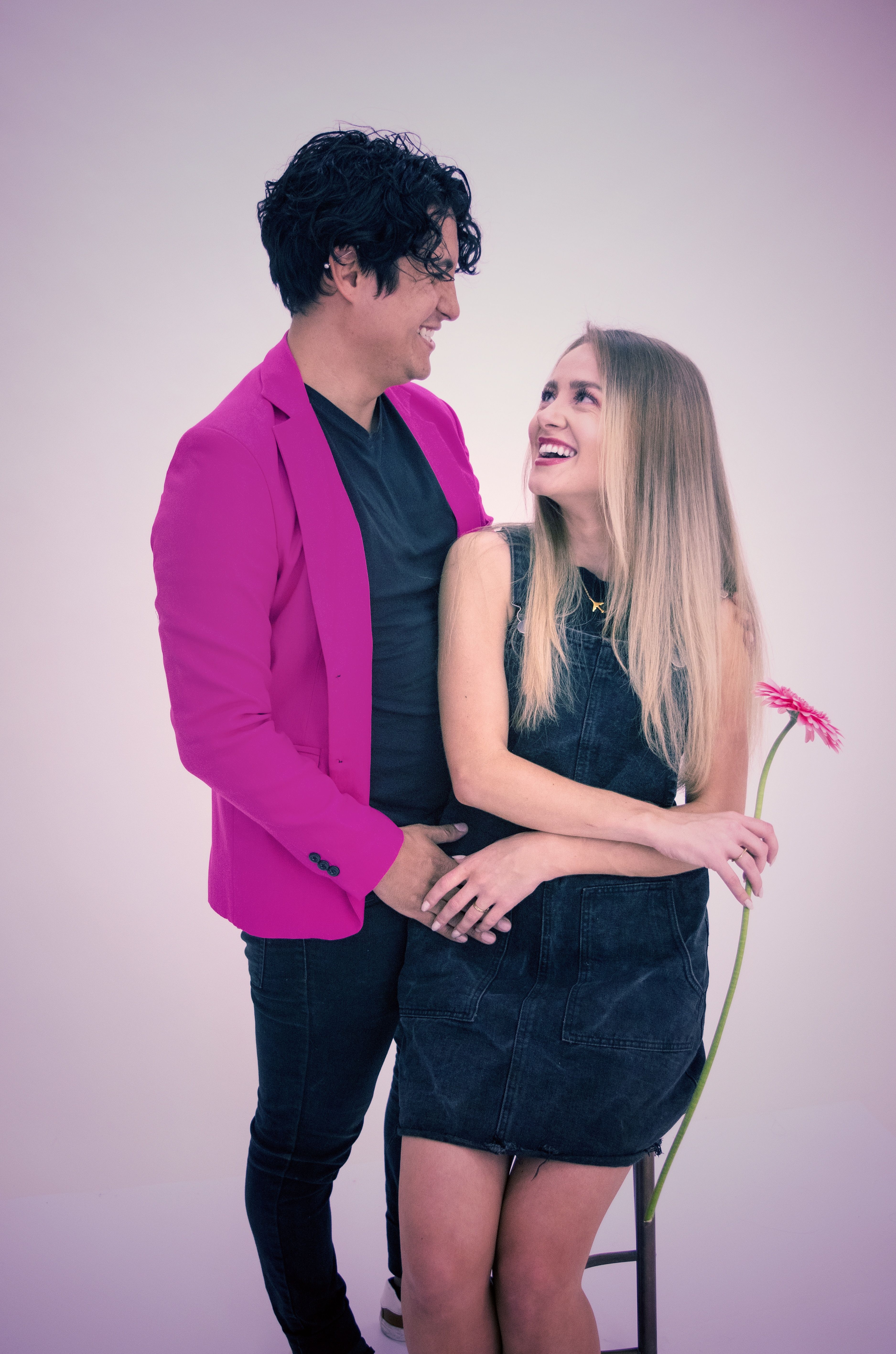 Joyful couple embracing and smiling with a pink flower, highlighting love and happiness.