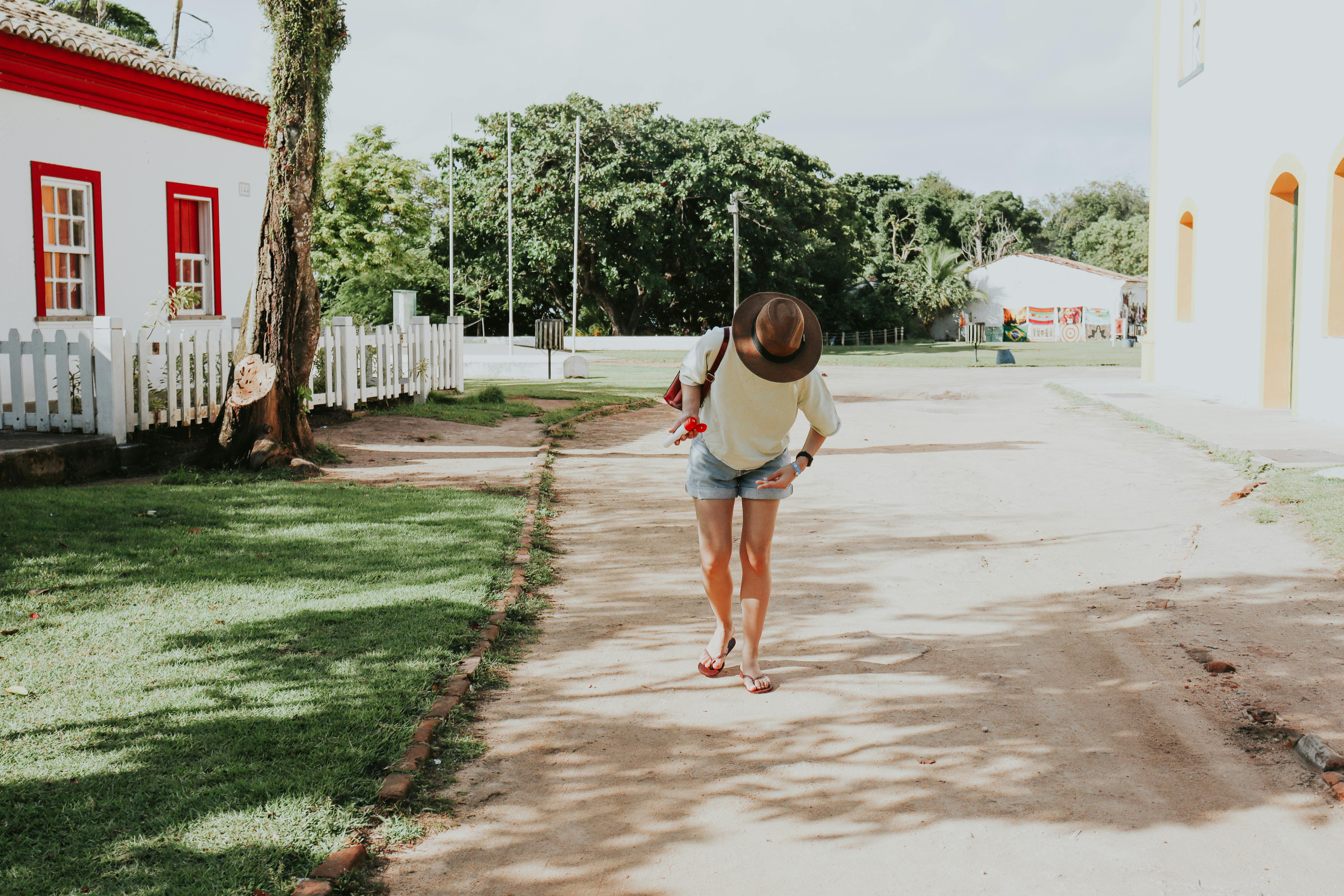 A woman in casual attire walks down a sunny street in Porto Seguro, Bahia, Brazil.