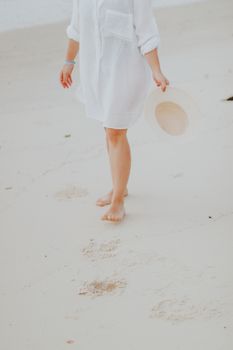 Woman walking barefoot on Porto Seguro beach, holding sun hat, serene summer moment.