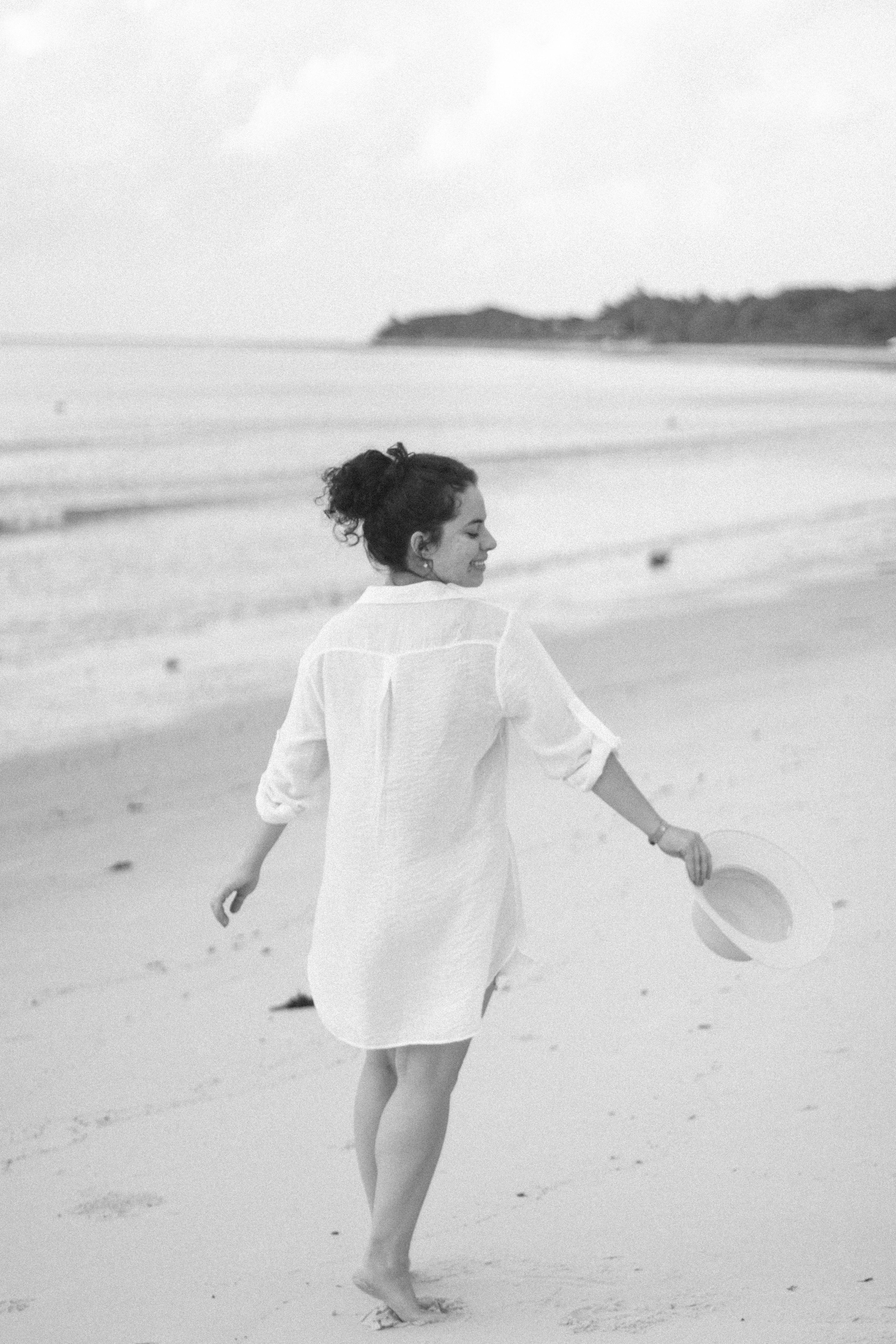 A woman walking on a tranquil beach in Porto Seguro, Brazil, holding a hat.