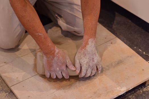 Close-up of hands kneading clay on a wooden board, showcasing a pottery-making process.