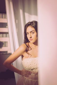 Elegant woman in a pink dress stands by a sunlit window in Buenos Aires.
