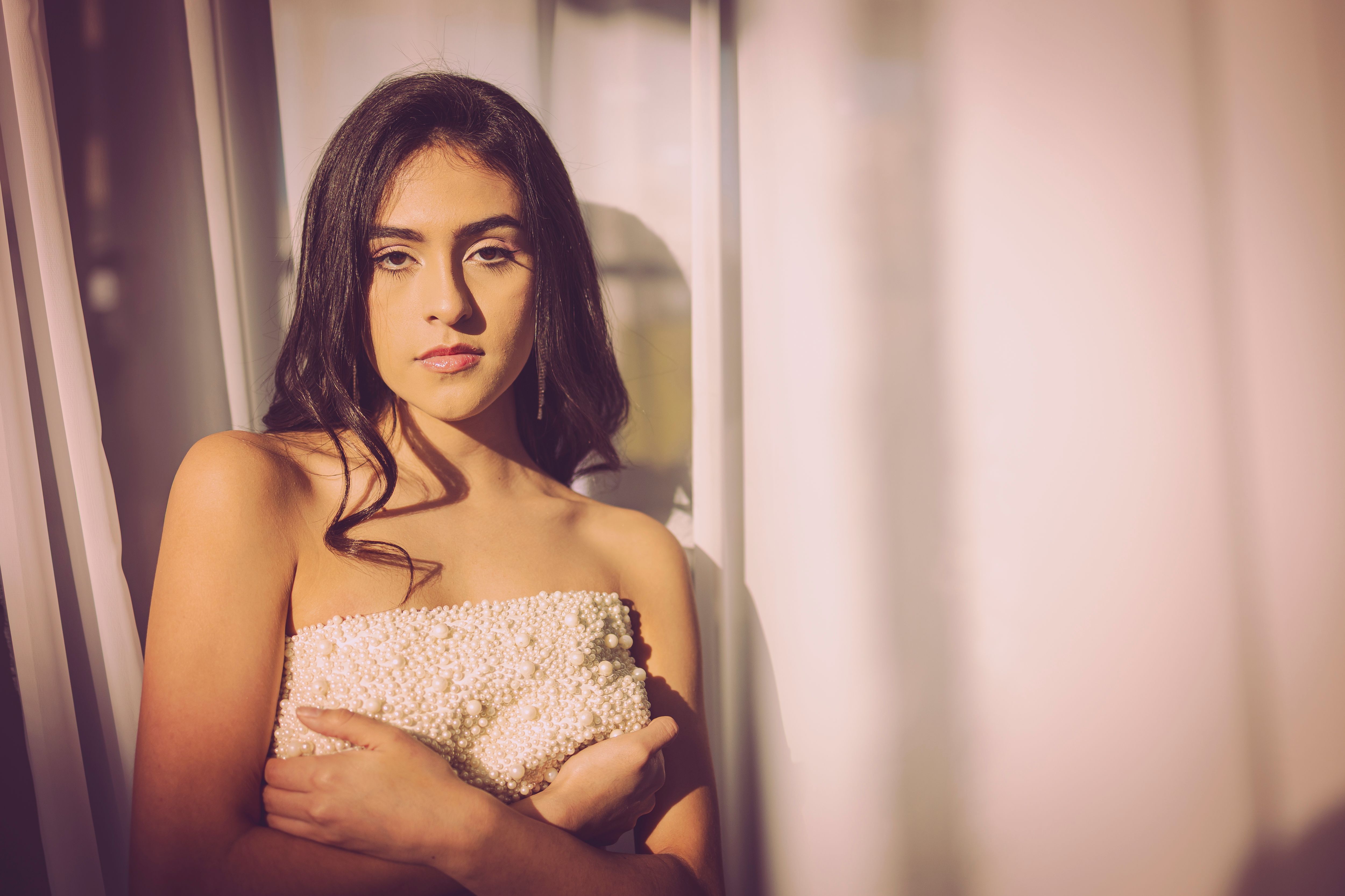 A beautiful woman poses gracefully by a window, bathed in warm sunset light.