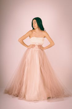Woman in a flowing pink gown posing elegantly in a studio setting.