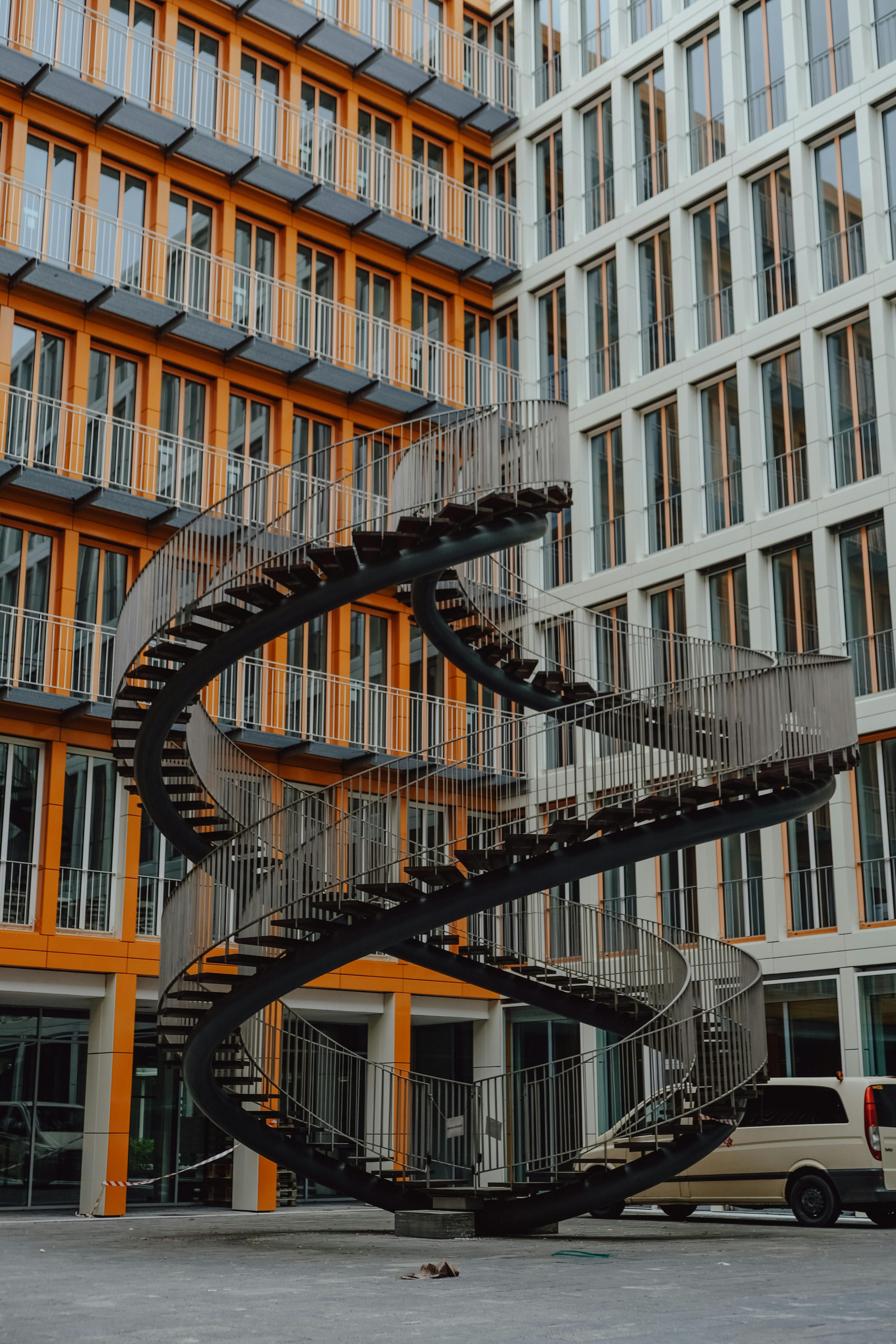 Artistic spiral staircase in a modern urban courtyard with vibrant orange facade.