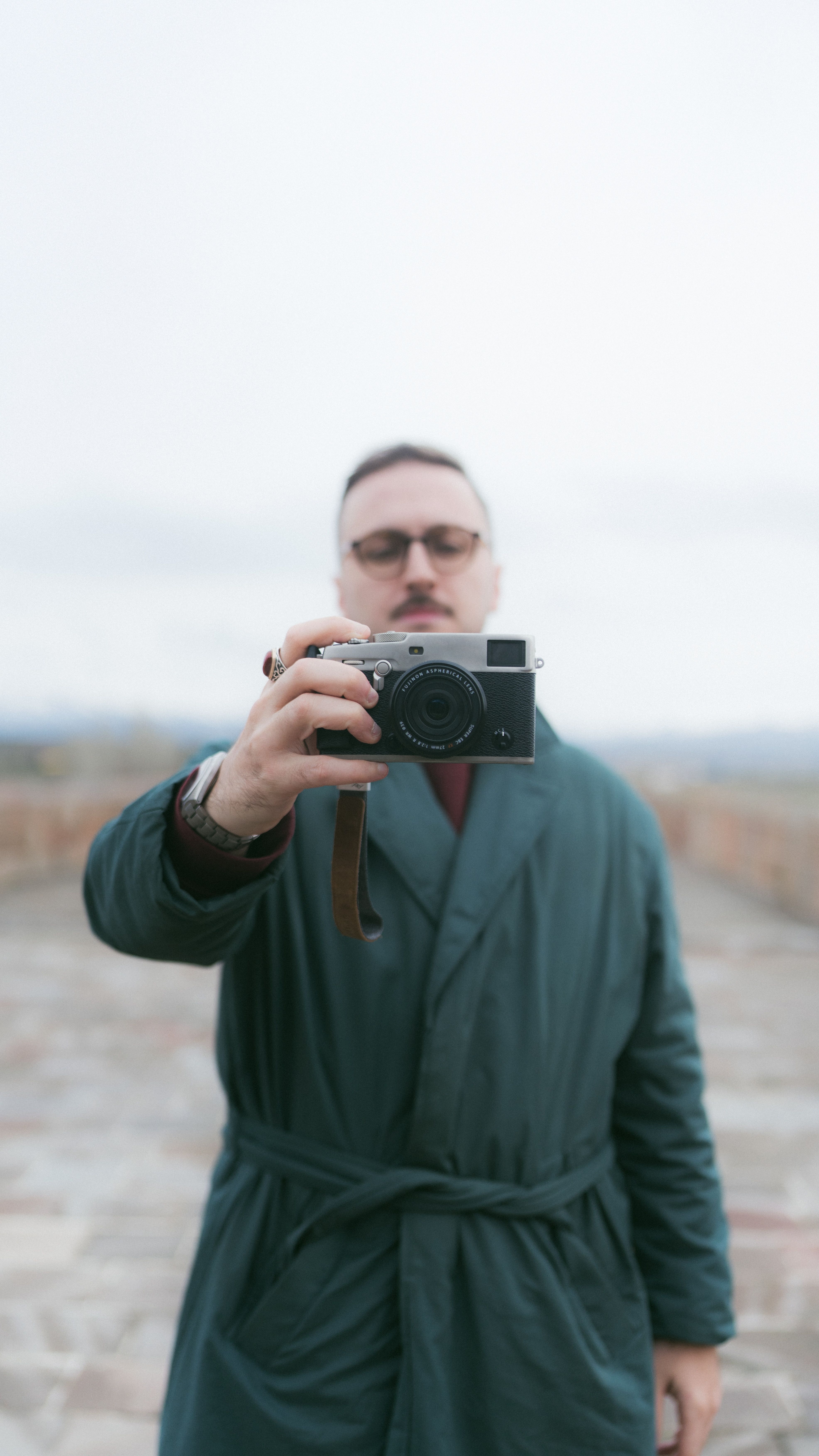 Man in green coat holding a camera, capturing a close-up self-portrait outdoors.