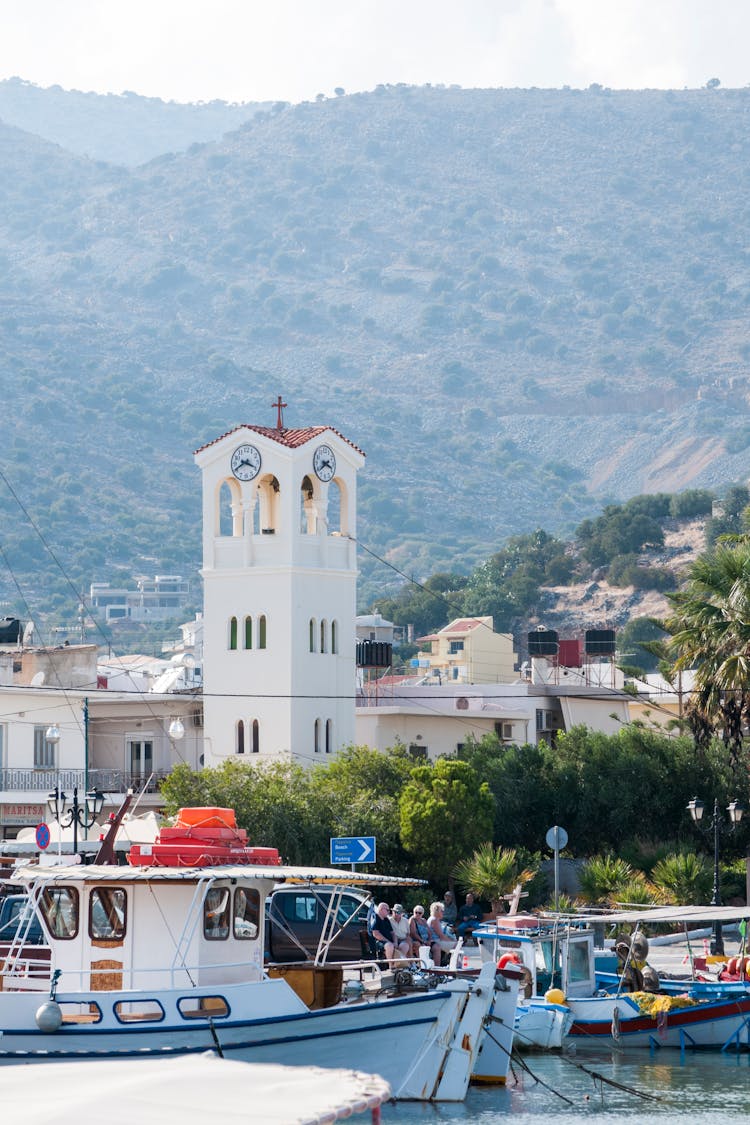 Old Tower Near Motorized Boats And Mountains In Summer