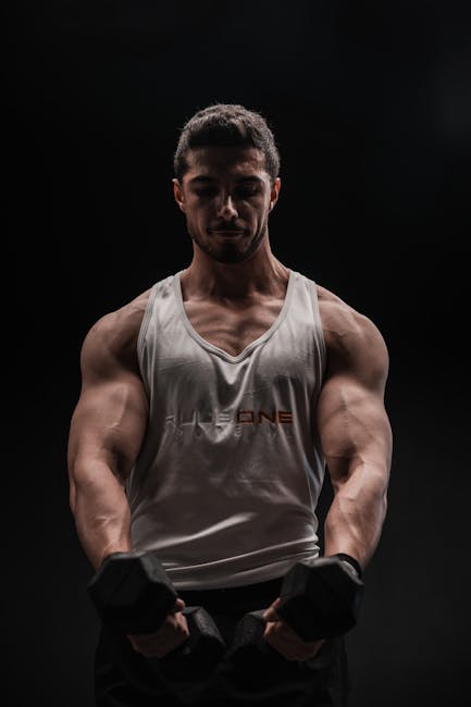Muscular man performing a bicep curl with dumbbells in low light.