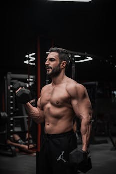 Fit male lifting dumbbells in a moody gym setting, showcasing strength and fitness.