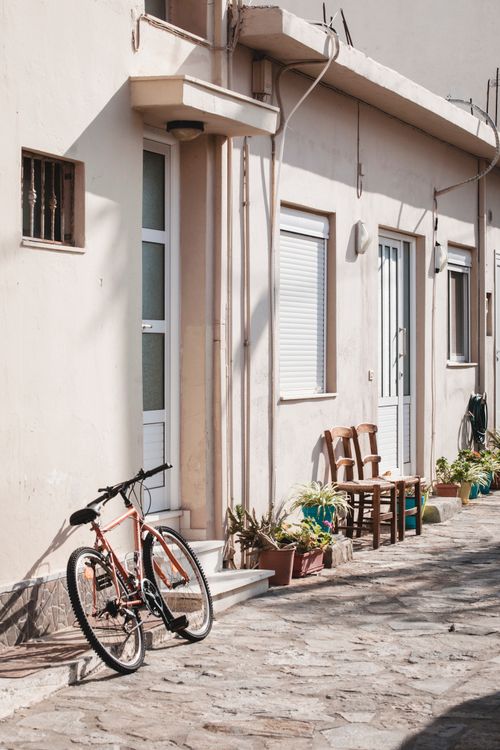 Free Quiet street scene featuring a bicycle and chairs against a traditional house facade. Stock Photo