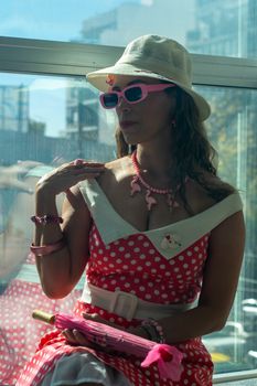 Chic woman in a retro polka dot dress with accessories, sitting by a window.