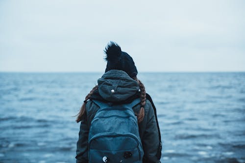 Вид сзади человека, несущего рюкзак, глядя в океан