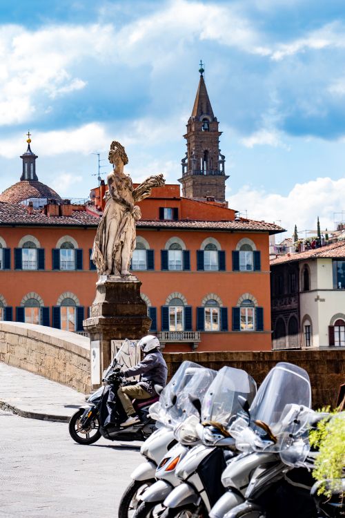 Free Street scene in Florence featuring a statue, motorbikes, and historic architecture. Stock Photo