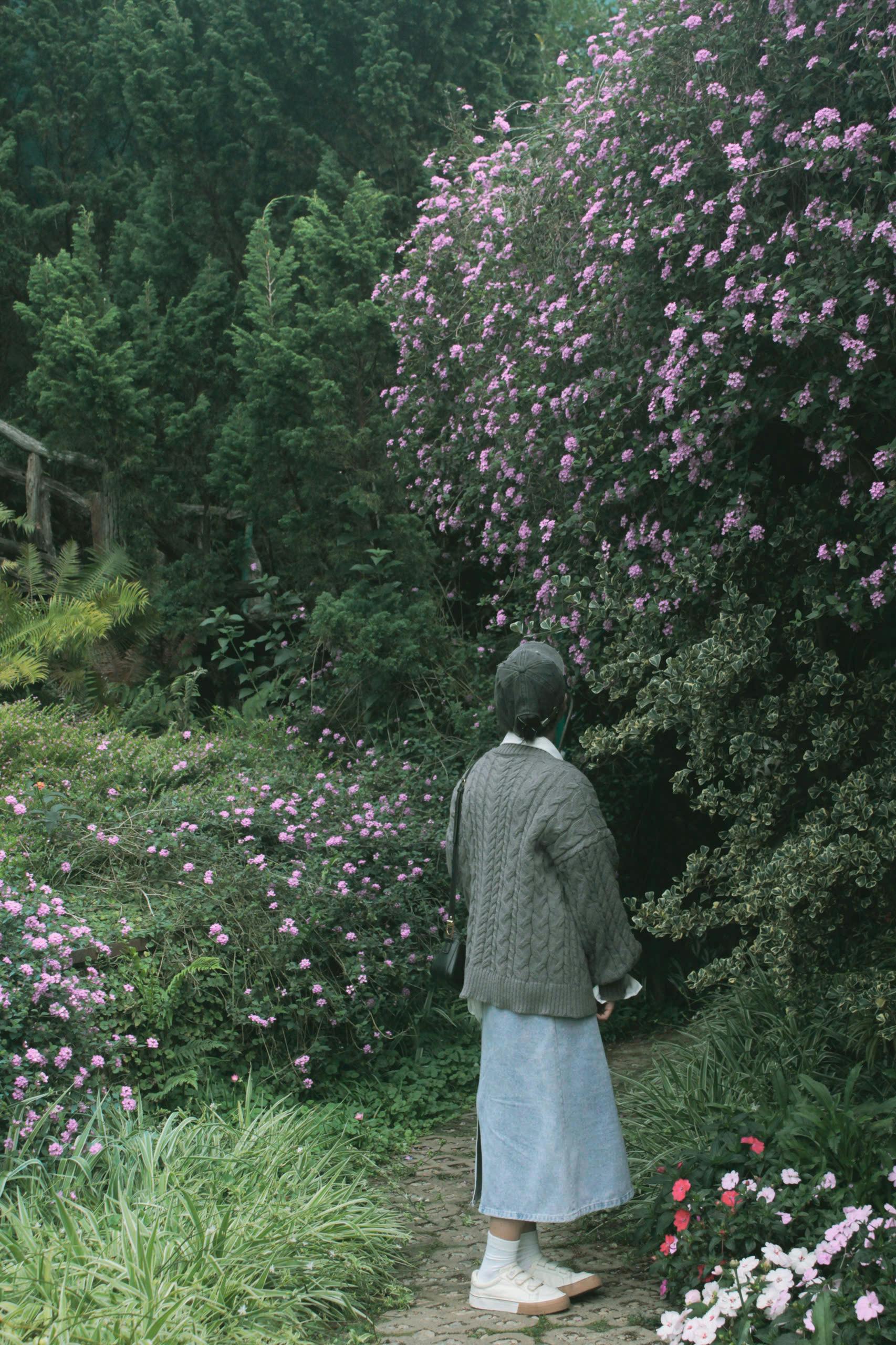 A woman enjoys a peaceful moment in a lush garden with blooming flowers.