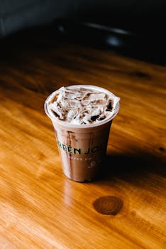 Iced coffee in a Green Joe's cup on a wooden table, perfect for a refreshing break.