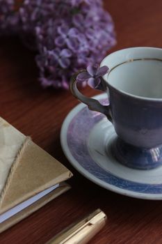 A vintage teacup with lilac flowers beside a notebook and pen on a wooden table.