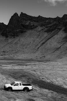 A black-and-white photo of a lone white pickup truck in a remote mountain setting.