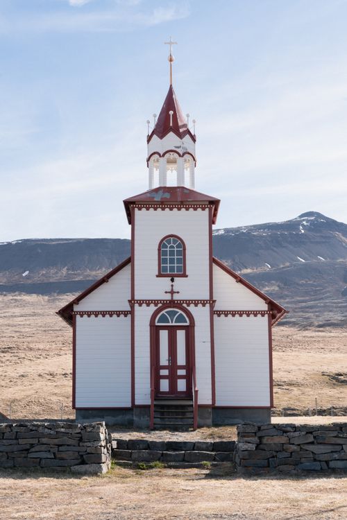 Free A picturesque white and red church set against a mountainous backdrop in Iceland. Stock Photo
