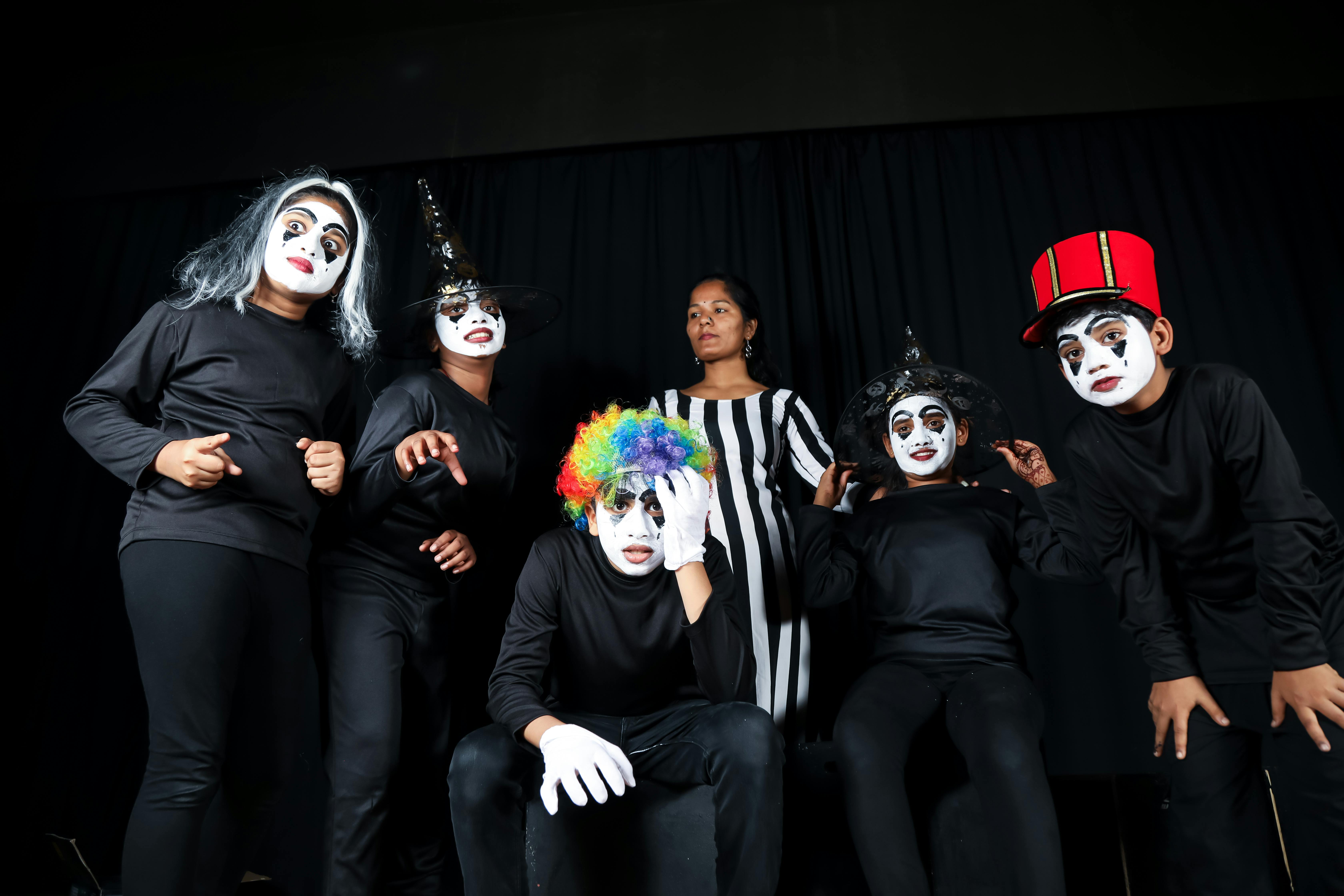 grátis Um grupo de jovens artistas em trajes e máscaras vibrantes apresentando uma performance teatral em um ambiente fechado. Foto profissional