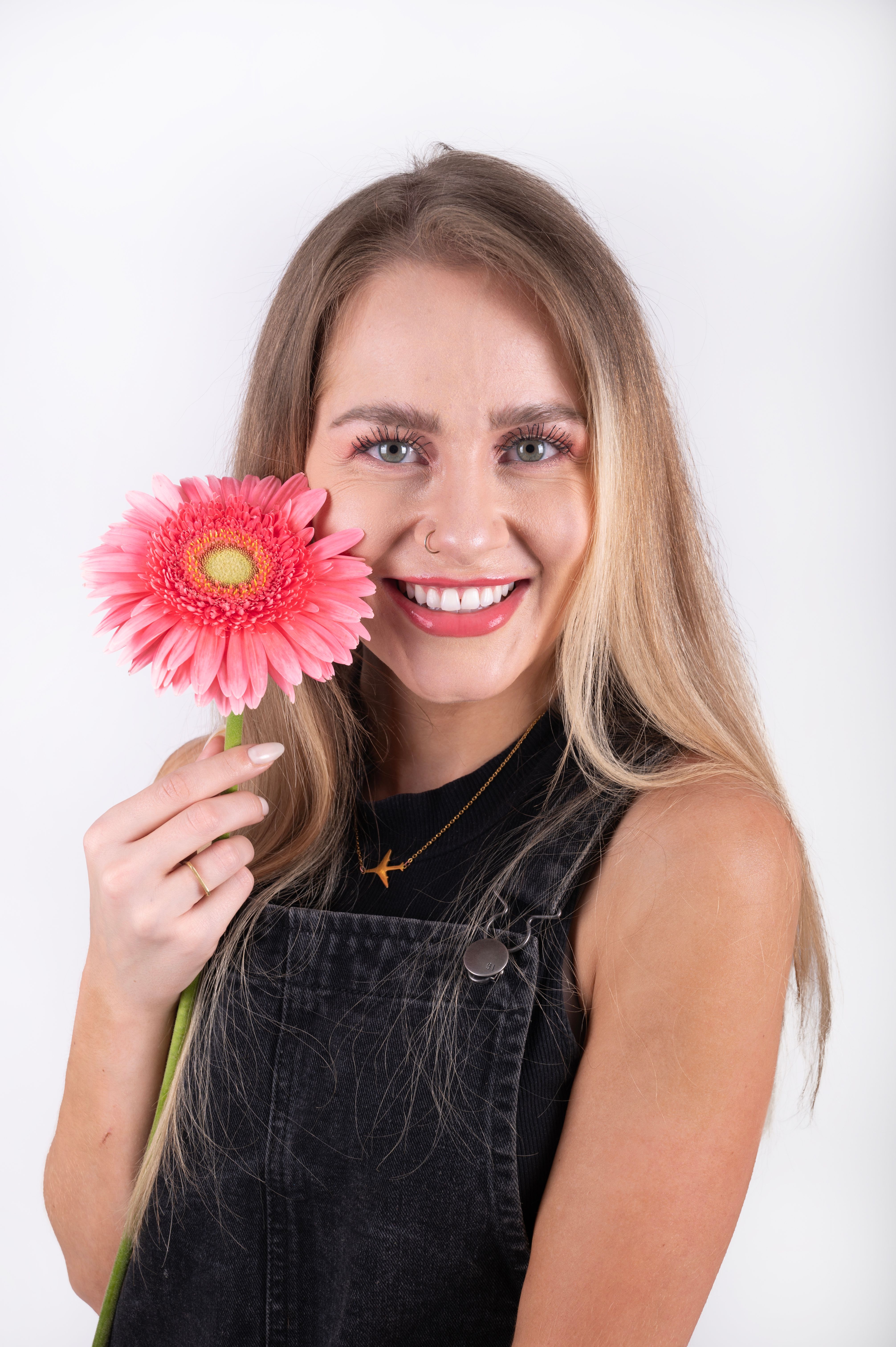 Portrait of a smiling woman with a pink gerbera daisy flower, perfect for lifestyle and beauty themes.