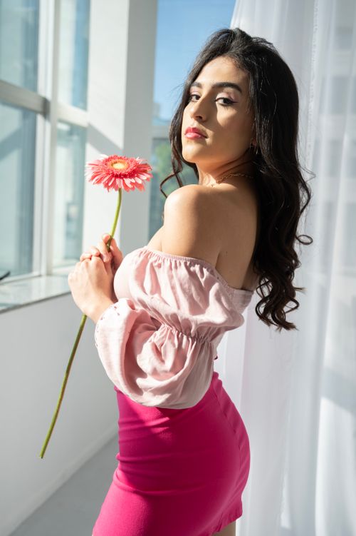 Free Portrait of a stylish woman in pink attire holding a pink daisy indoors with natural light. Stock Photo