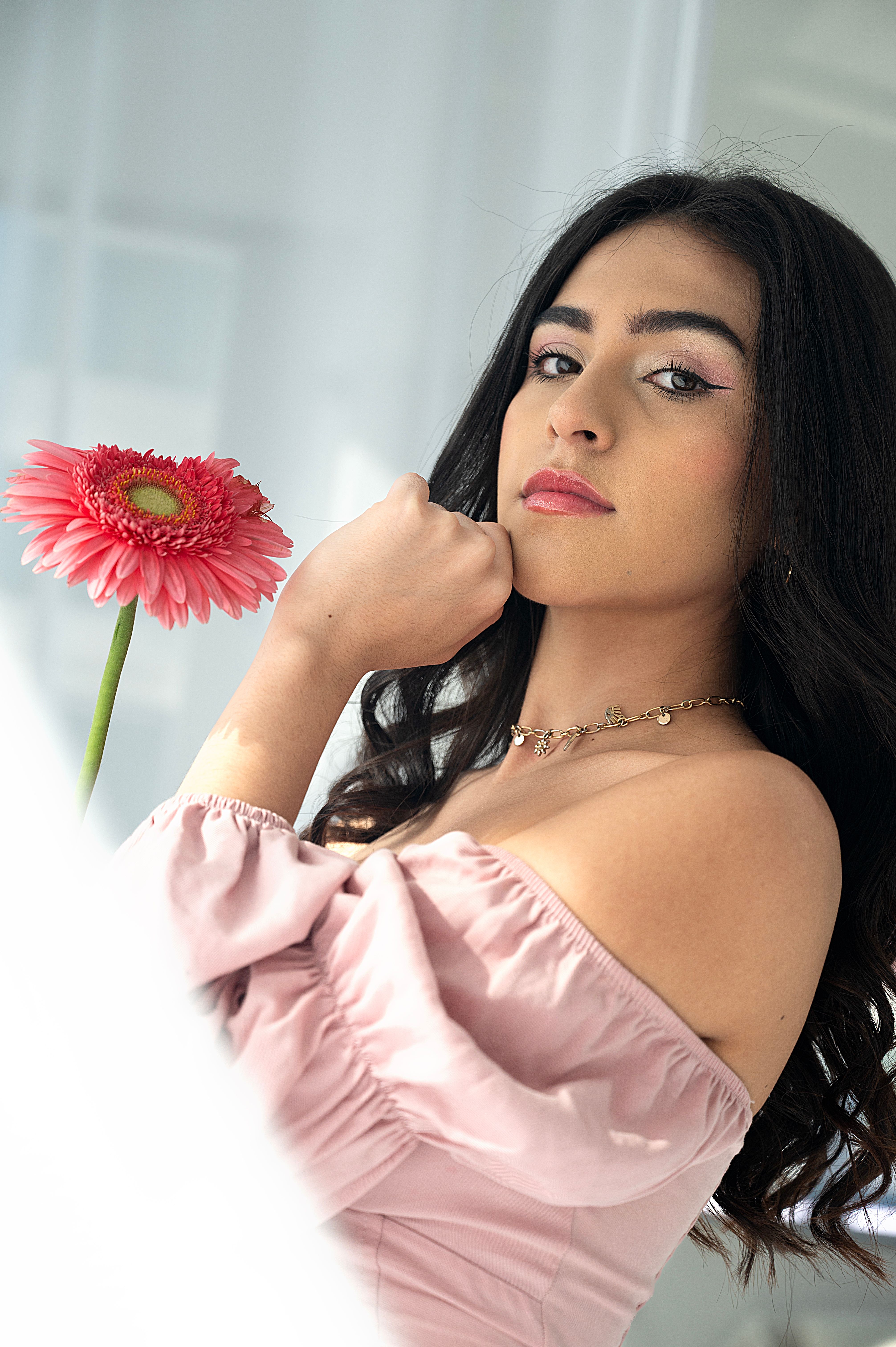 Chic portrait of a woman in a pink dress with a pink flower, taken indoors.