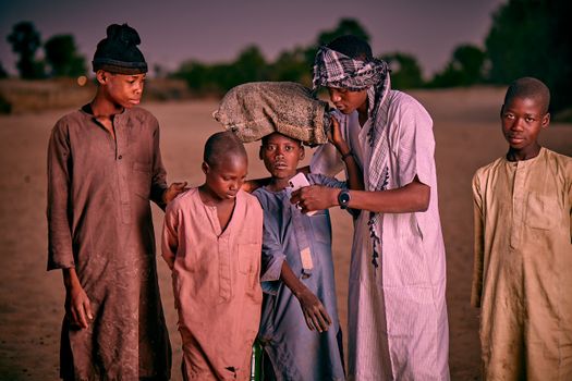 Five boys wearing traditional clothing stand together at sunset. Candid moment outdoors.