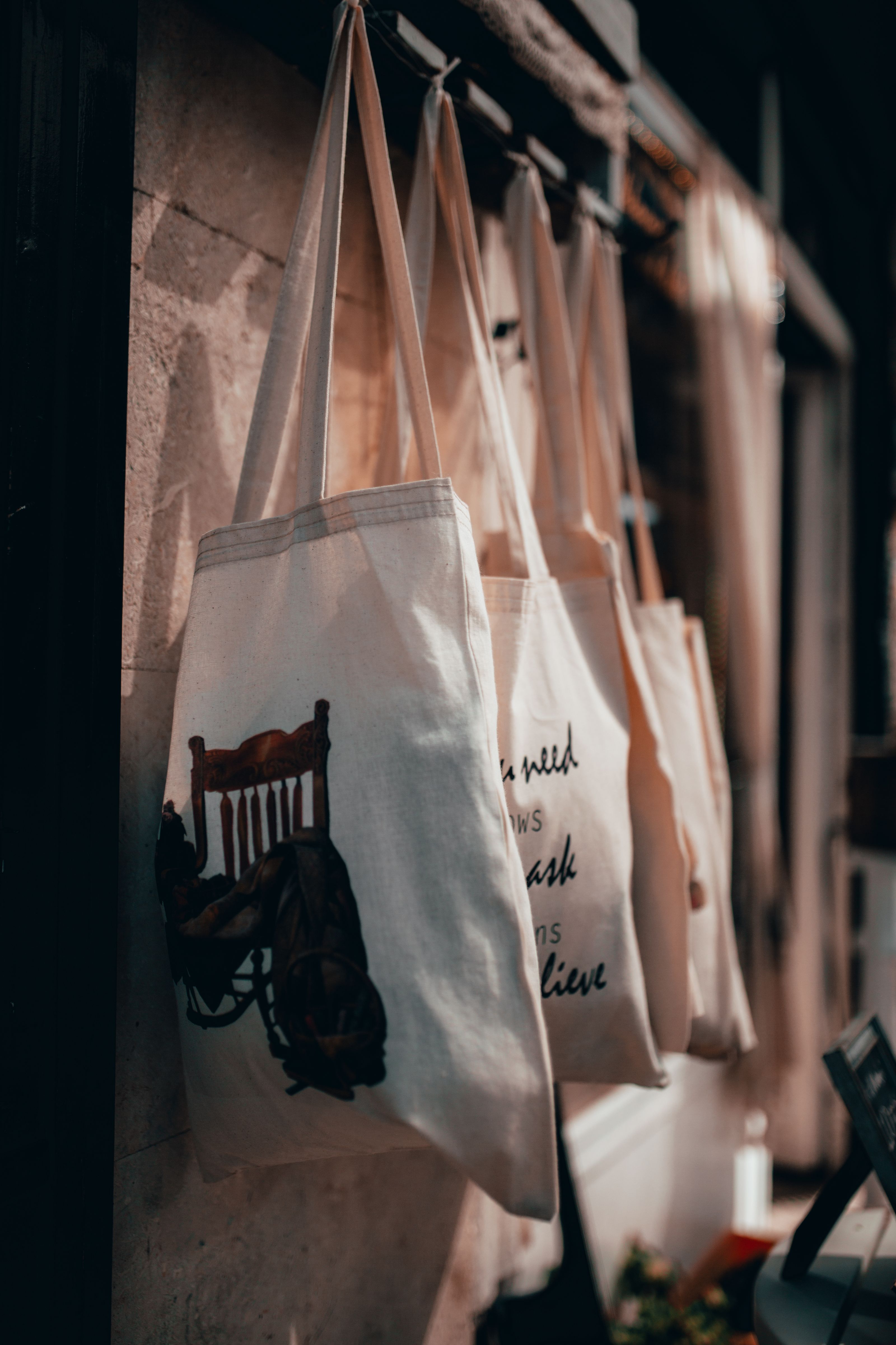 Close-up de sacolas de lona penduradas em um suporte em um interior de loja com iluminação aconchegante.