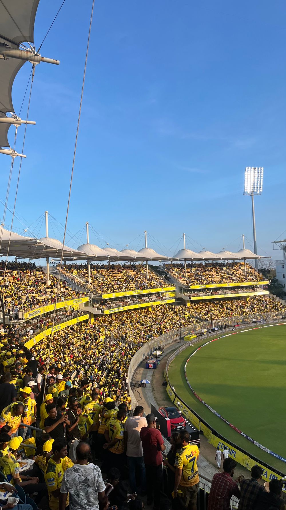 Packed stadium crowd in bright yellow jerseys cheering under a clear blue sky