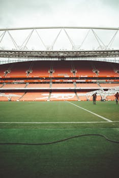 Wide view of empty Emirates Stadium highlighting architecture and field on a cloudy day.