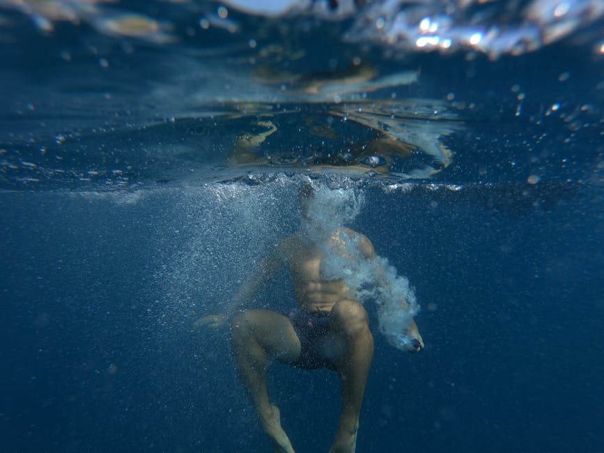 A person photographed diving underwater in a deep blue ocean creating bubbles.