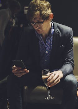 A young man in a stylish suit using his phone while holding a glass of champagne in a chic lounge.