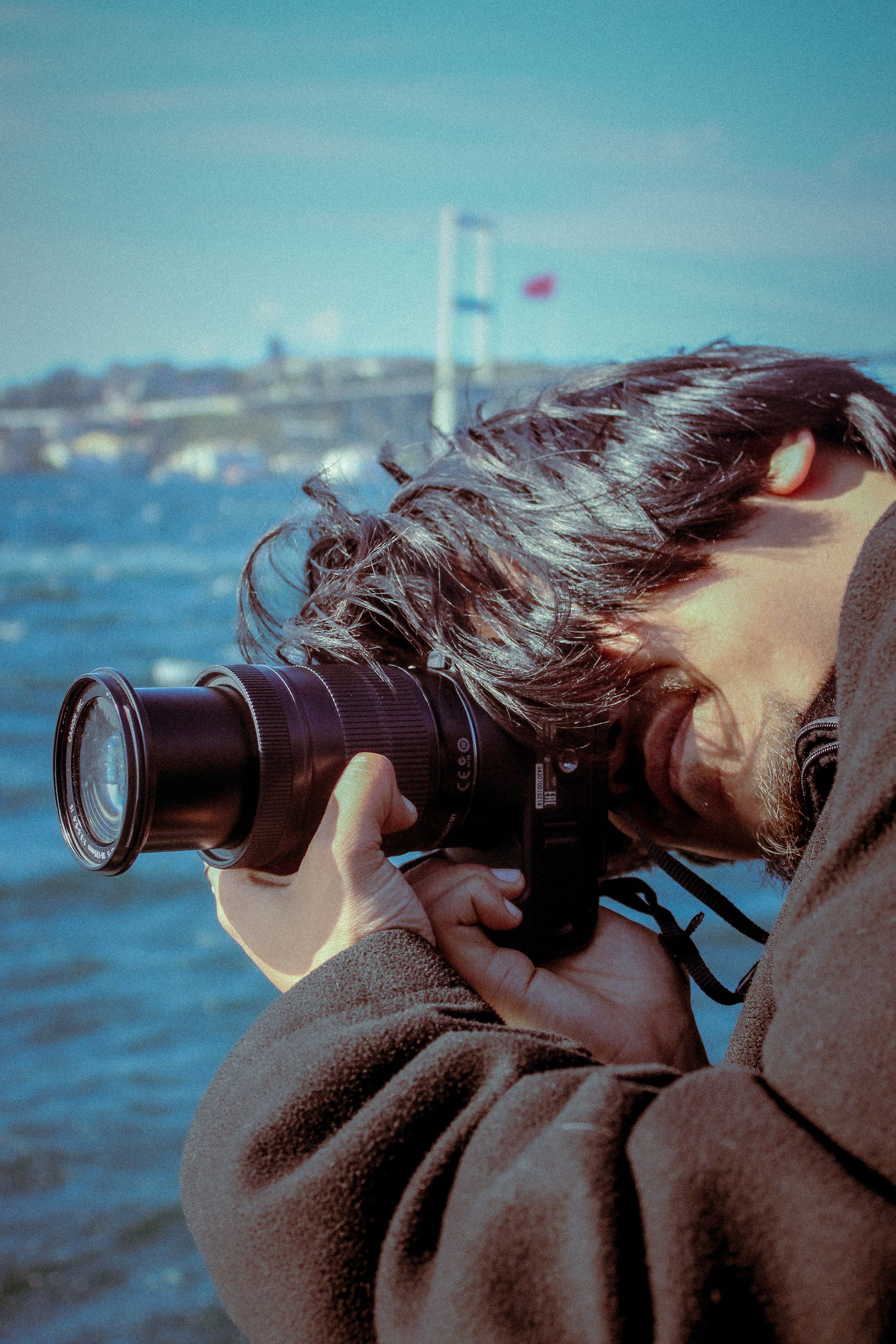 A person taking photos by the sea with a DSLR camera on a sunny day.