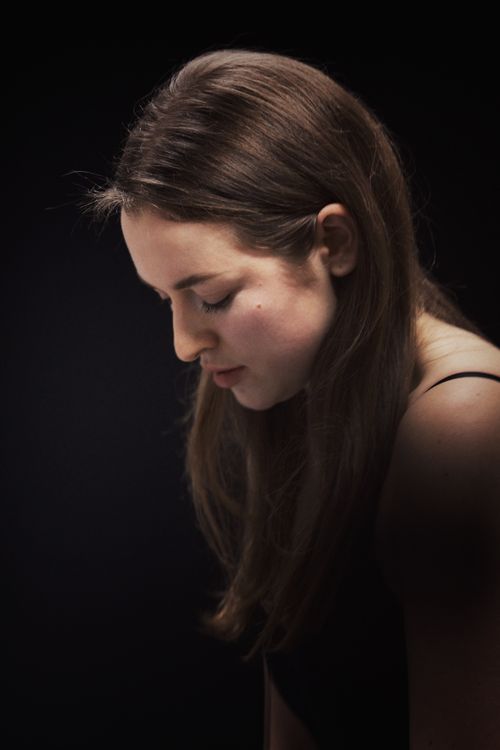 Free Artistic portrait of a young woman gazing down in quiet reflection against a dark background. Stock Photo