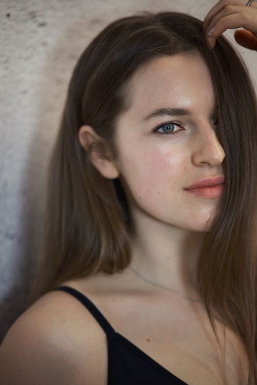 Free Young woman with long brown hair smiles gently indoors. Natural lighting and relaxed expression. Stock Photo