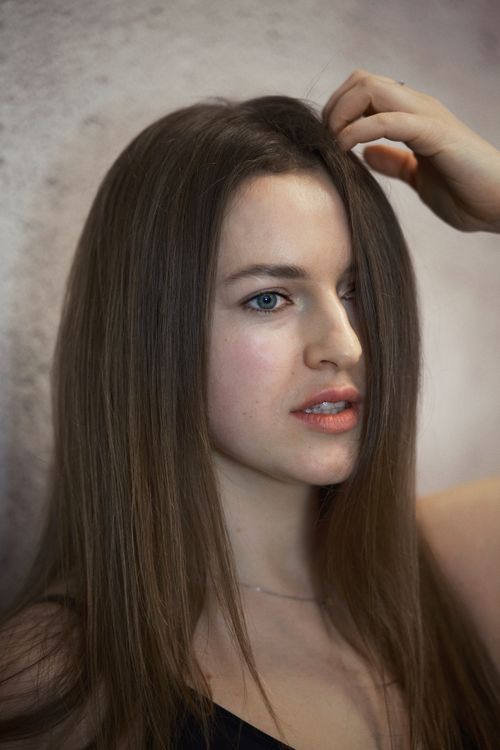 Free Close-up portrait of a young woman with long brown hair touching her head. Stock Photo