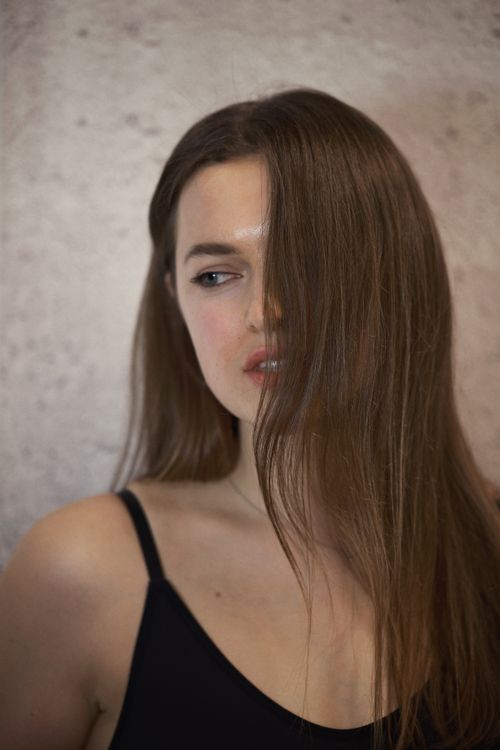 Free Close-up portrait of a woman with long brown hair covering half her face, wearing a black top. Stock Photo