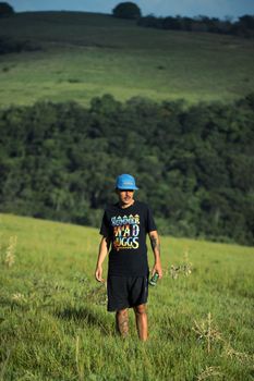 Man with tattoos and cap walking in a serene green field during the day.