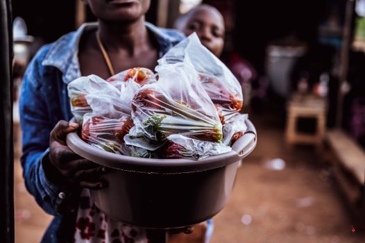 Woman selling fresh vegetables in plastic bags at outdoor market, showcasing local trade.